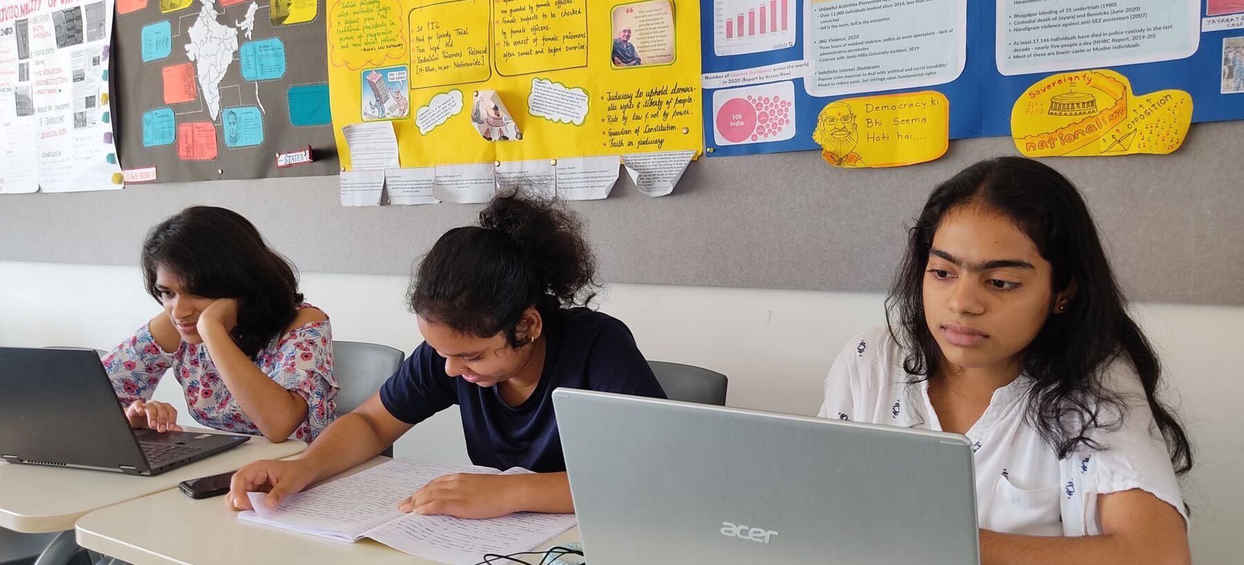 Three students working on laptop in classroom