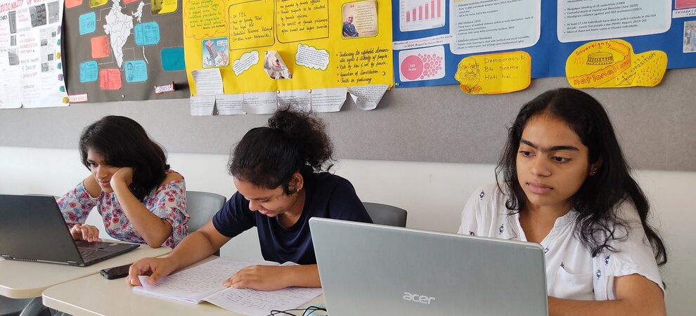 Three students working on laptop in classroom